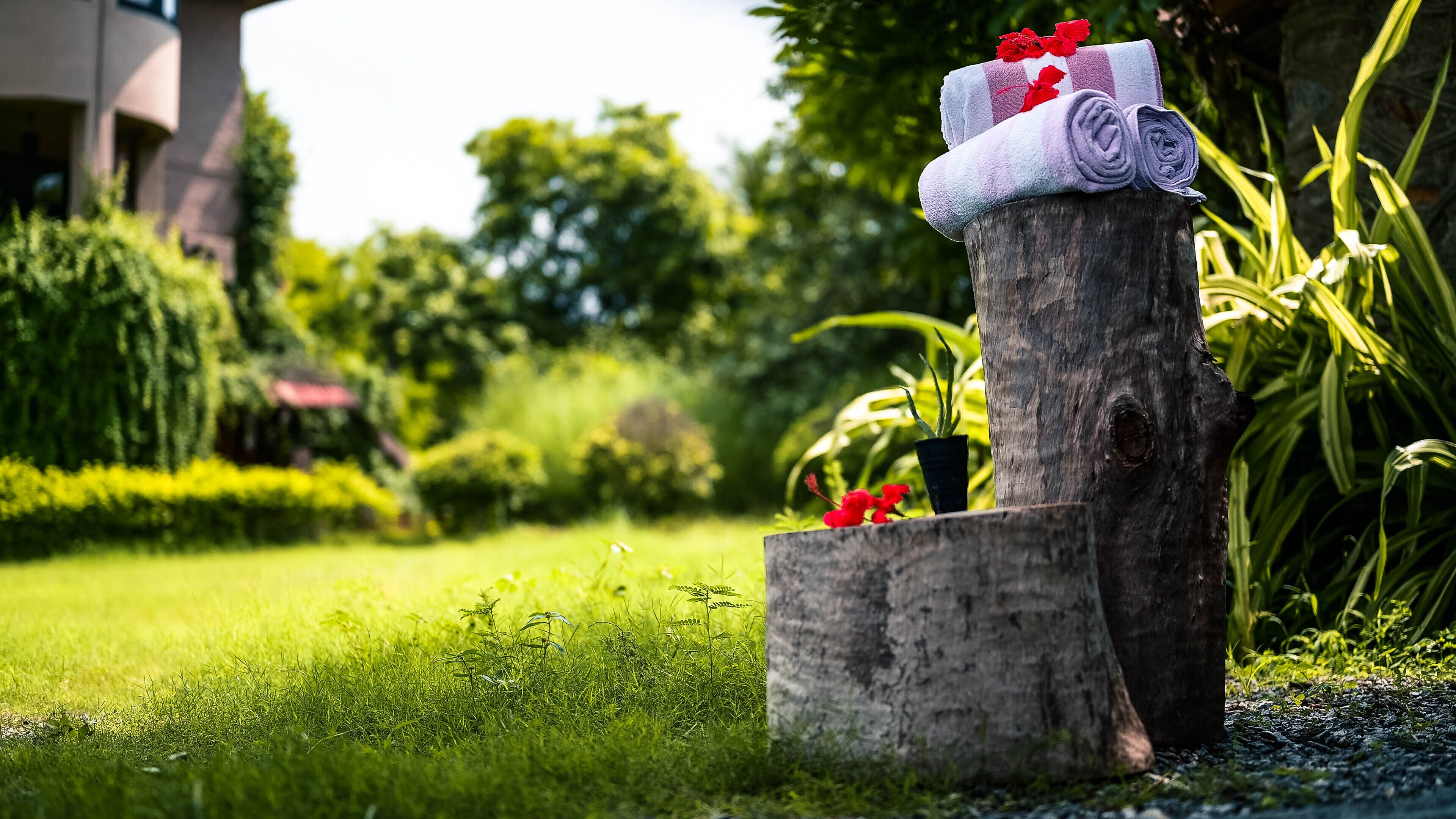 A wooden post with rolled towels and red flowers, surrounded by lush greenery and a well-maintained lawn.