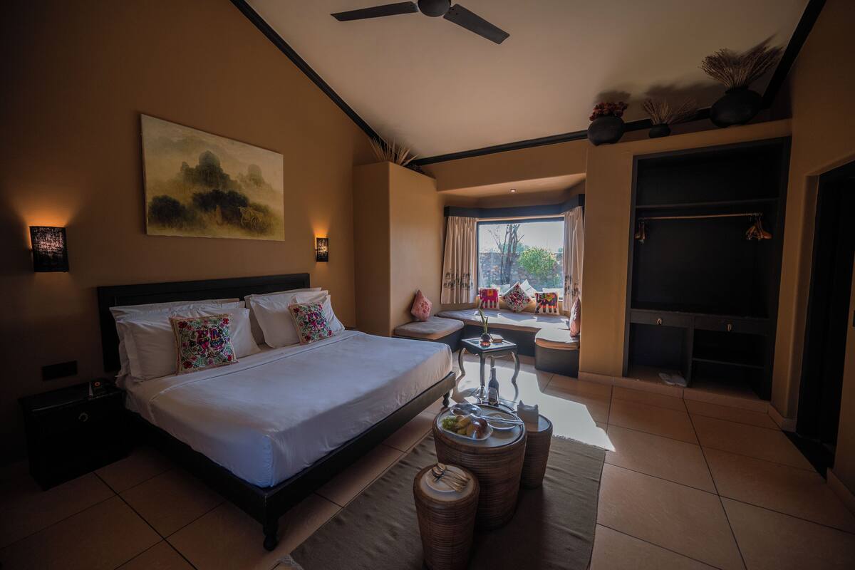 A bedroom with a large bed, bedside tables, a small table with a vase, and a view of the outdoors.