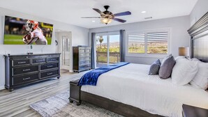 Un dormitorio con cama, ventilador de techo, televisor, cómoda y vistas al exterior.