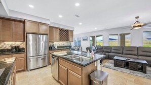 Una cocina moderna con electrodomésticos de acero inoxidable, una isla central con pileta y un comedor con sofá de cuero oscuro y una mesa de centro.
