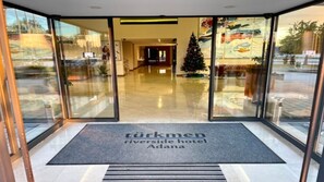 A hotel entrance with glass doors, a Christmas tree, and a sign reading "Türkmen Riverside Hotel Adana".