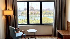 A hotel room with a large window offering a view of a cityscape and a river. - Turkmen Riverside Hotel (Adana)