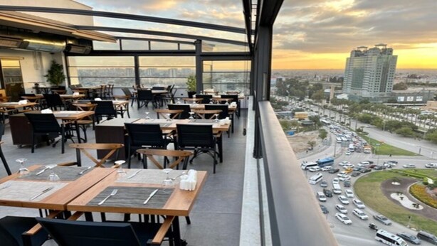 An outdoor dining area with tables and chairs, overlooking a cityscape and a busy road. - Turkmen Riverside Hotel (Adana)