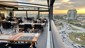 Un espace de restauration en plein air, avec des tables et des chaises, offrant une vue sur le paysage urbain et une rue animée.