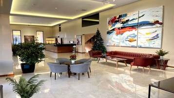 A spacious lobby with a reception desk, a red sofa, grey armchairs, and a Christmas tree.