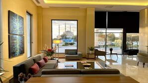 A modern hotel lobby with a sofa, armchairs, and a coffee table. There is a large window with a view of a mosque and a parking lot. - Turkmen Riverside Hotel (Adana)