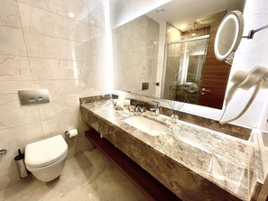 A bathroom with a marble sink, a toilet, a mirror with a built-in phone, and a shower area.
