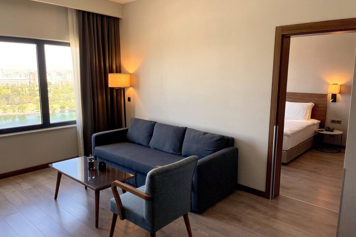 A hotel room with a sofa, a small table, a chair, a bed, and two wall lamps.
