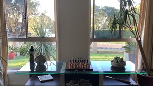A chessboard on a glass-top desk with a book beside it, a vase, and a plant in a pot. - Maggie’s Nest Come & Rest (Killarney Vale)
