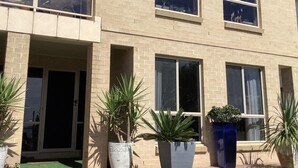 A two-story building with a brick facade, large windows, and potted plants in front. - Maggie’s Nest Come & Rest (Killarney Vale)