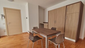A room with a wooden table, four chairs, a wardrobe, and a small kitchenette. - Apartment in an apartment complex (Schio)