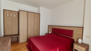 A bedroom with a wooden wardrobe, a bed with a red bedspread, a bedside table with a lamp, and a wooden nightstand. - Apartment in an apartment complex (Schio)