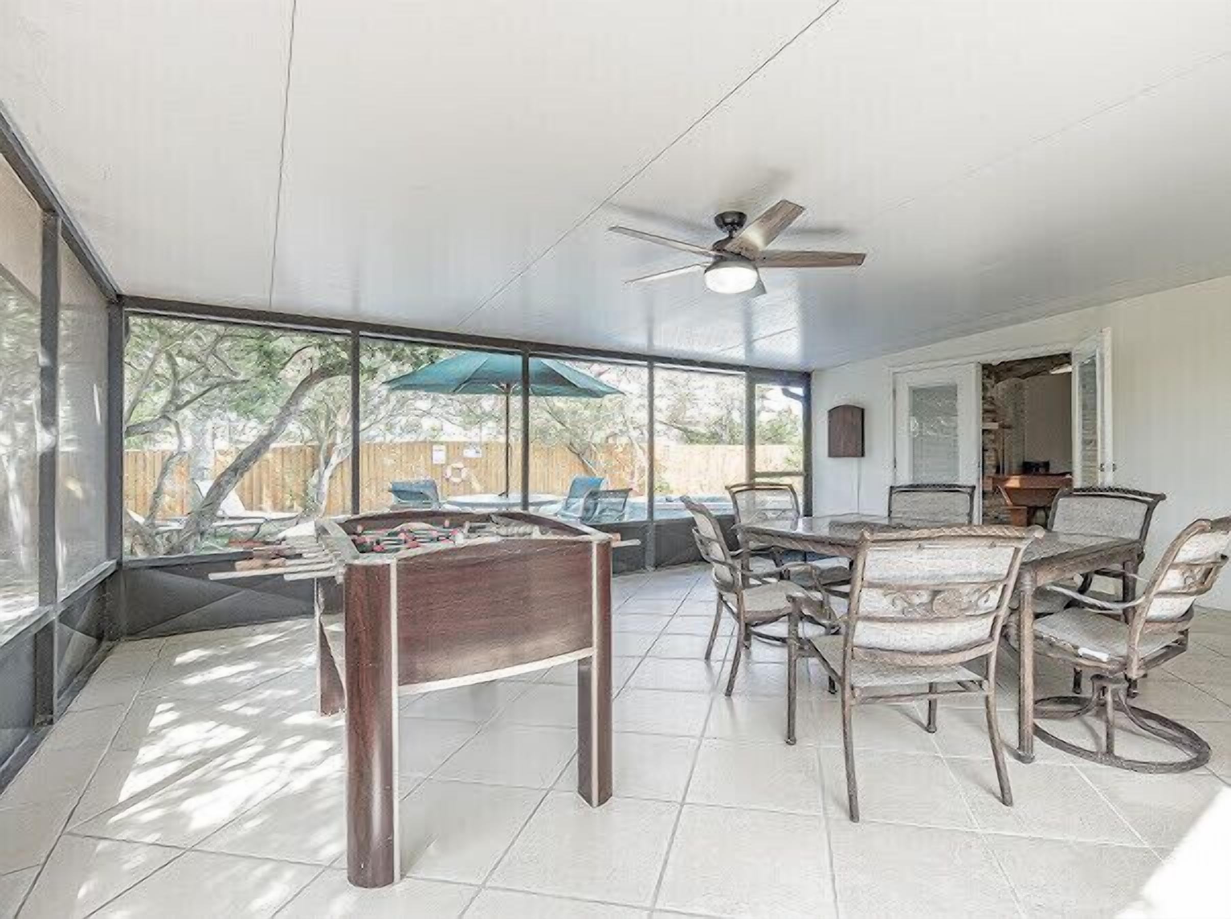 A spacious patio with a pool table, dining table, and chairs, large windows offering a view of the backyard.