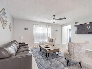 A living room with a gray sofa, a wooden coffee table, a patterned armchair, and a ceiling fan. - Perfect Location Heated Pool House (Tampa)