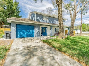 A two-story house with a blue garage door, a front porch, and a driveway leading to the entrance. - Perfect Location Heated Pool House (Tampa)