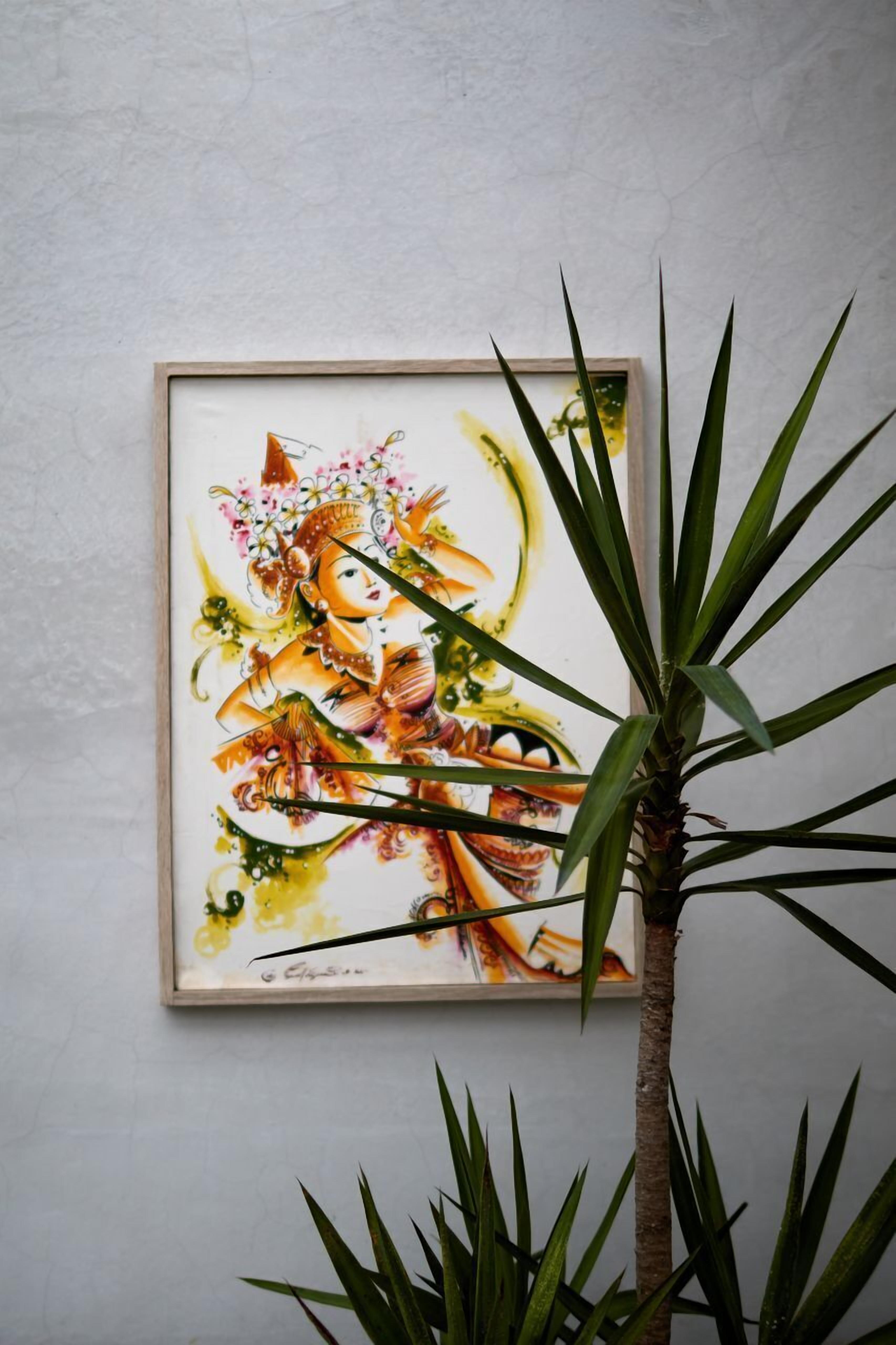 A framed artwork on a wall with a plant in the foreground.