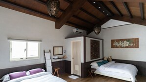 Quarto com duas camas, piso de madeira, janela, ar-condicionado, uma pequena mesa e um objeto decorativo na parede.