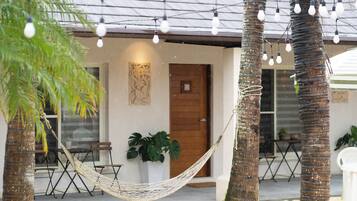A hammock tied between palm trees, a wooden door, and a table with chairs outside a building.