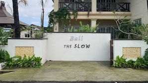 Um edifício com uma placa que diz "Bali The Slow" e uma área de entrada coberta com plantas.