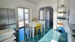 Une cuisine moderne avec des meubles blancs, une table à manger entourée de chaises jaunes et un sol carrelé de carreaux bleus.