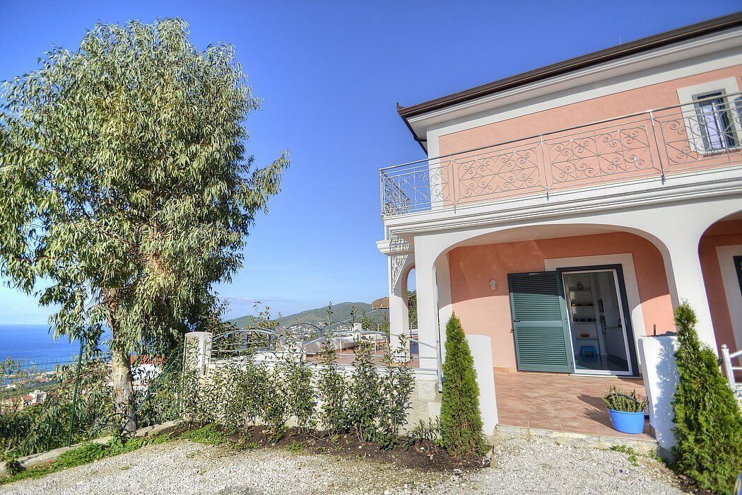 Un edificio a due piani con un balcone, una porta e vista sul mare.