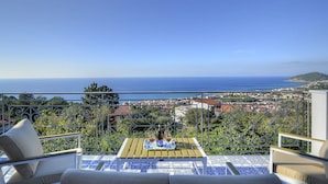 Une terrasse avec une table dressée pour deux personnes, offrant une vue sur une ville côtière et la mer.