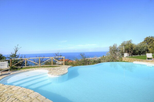 Une piscine à bord incurvé, une terrasse en bois et une vue sur la mer.