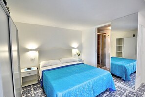 Une chambre d’hôtel avec un grand lit, une table de chevet, une armoire et une salle de bain visible à travers une porte ouverte.