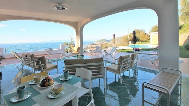 Un espace de restauration extérieur baigné de soleil, avec vue sur la mer, aménagé avec des tables et des chaises, et une piscine en arrière-plan.