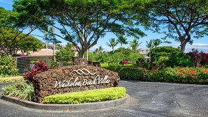 Señal de Waikoloa Beach Villas con jardín ajardinado y árboles tropicales.