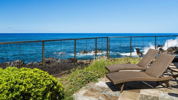 Een balkon met rieten stoelen met uitzicht op een rotsachtige kustlijn en de oceaan.