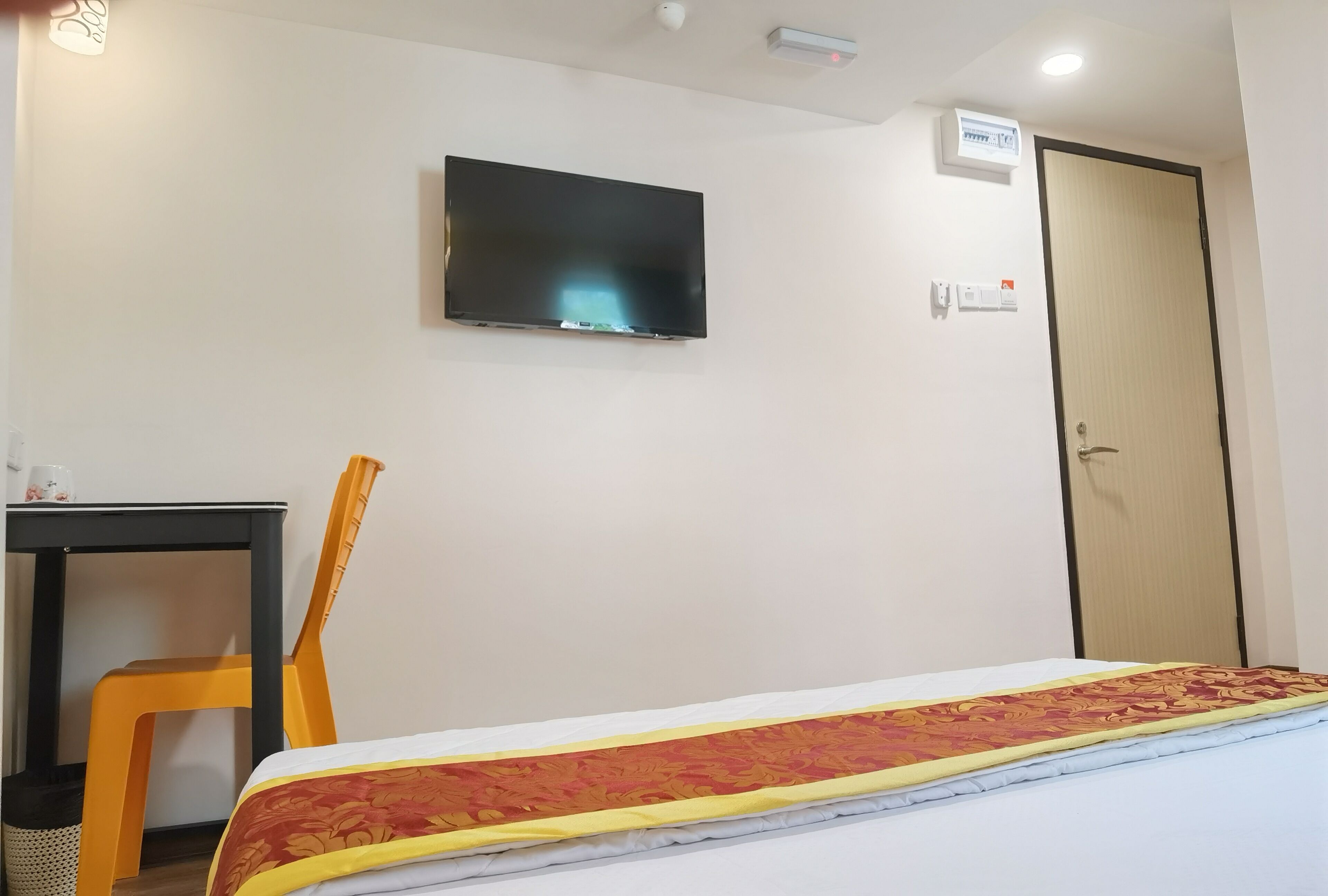 A hotel room with a bed, a television mounted on the wall, a desk with a chair, and a door.