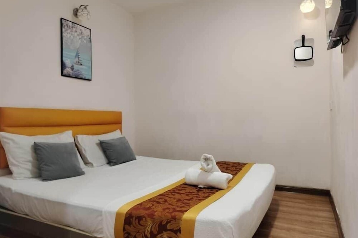 A hotel room with a bed, a headboard, a wall-mounted light fixture, and a painting.