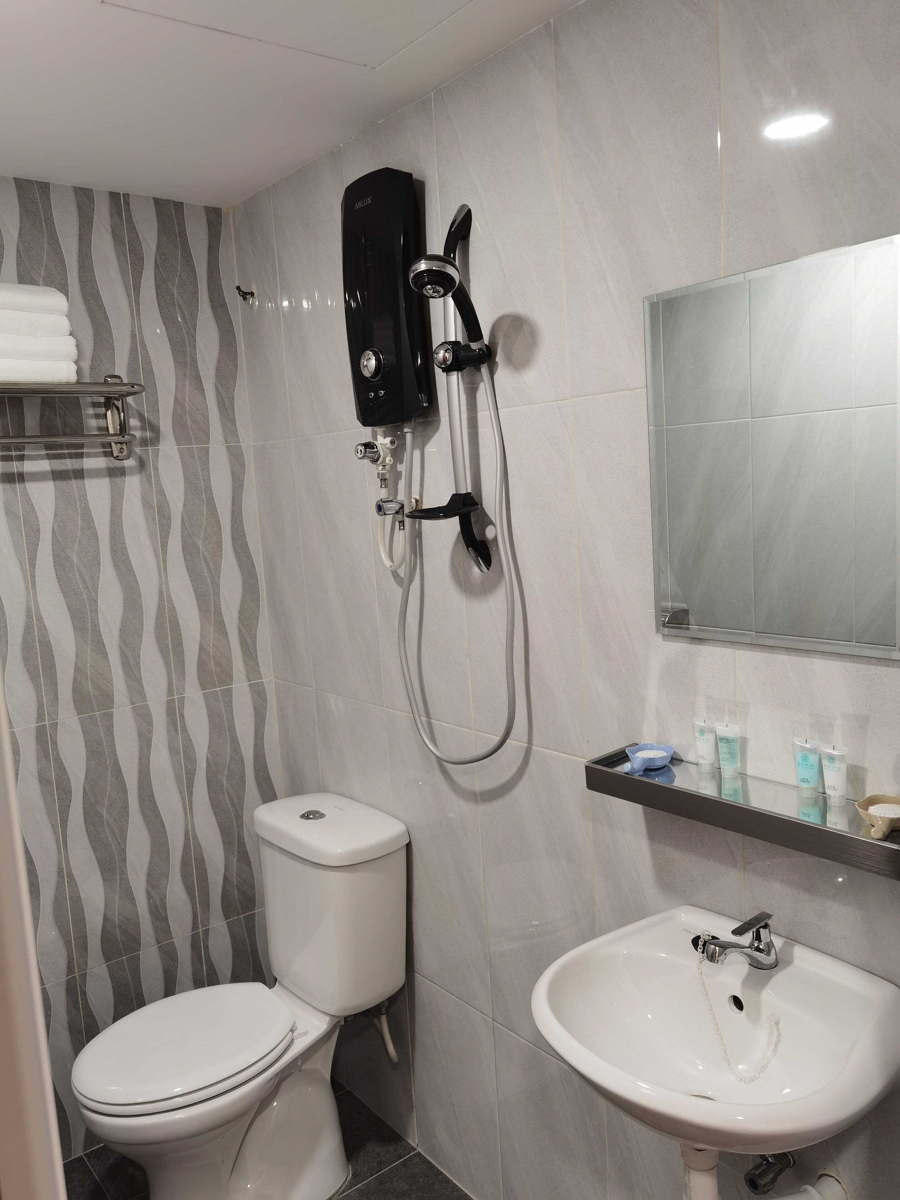 A bathroom with a toilet, a sink, a shower unit, and a mirror.
