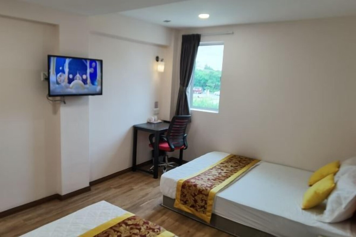 A hotel room with two beds, a desk, a chair, a TV, and a window with curtains.