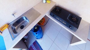 A compact kitchen with a sink, stove, and gas cylinder. - Next Trip Homestay Jogja (Kalasan)