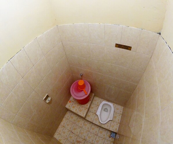 A small, enclosed bathroom with a toilet, a pink basin, and a red container.