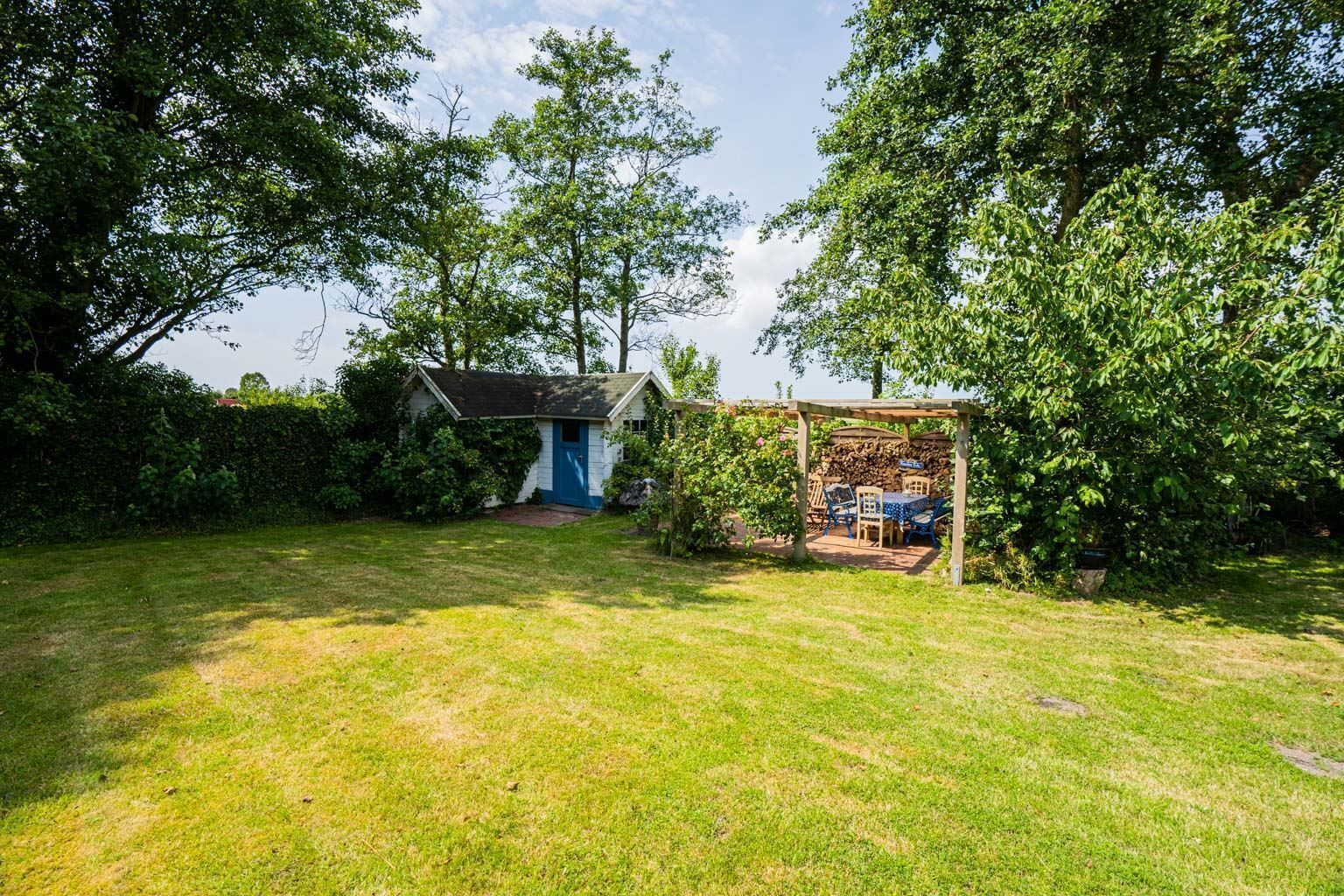 Ein Garten mit einem kleinen Schuppen, einer überdachten Sitzgelegenheit und einer Rasenfläche.