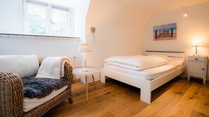 A cozy bedroom with a bed, a chair, a small table, and a lamp. - Vacation home "Seeräuberhäuschen" (ID 442) (Tating)