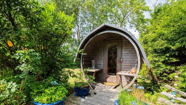 A small, round wooden structure with a door, a small table, and a bench outside. - Vacation home "Seeräuberhäuschen" (ID 442) (Tating)