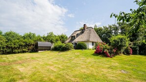 A thatched-roof house with a well-maintained lawn and surrounding greenery. - Vacation home "Seeräuberhäuschen" (ID 442) (Tating)
