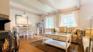 A cozy living room with a fireplace, a dining area with a table and chairs, and a sofa with plaid cushions. - Vacation home "Seeräuberhäuschen" (ID 442) (Tating)