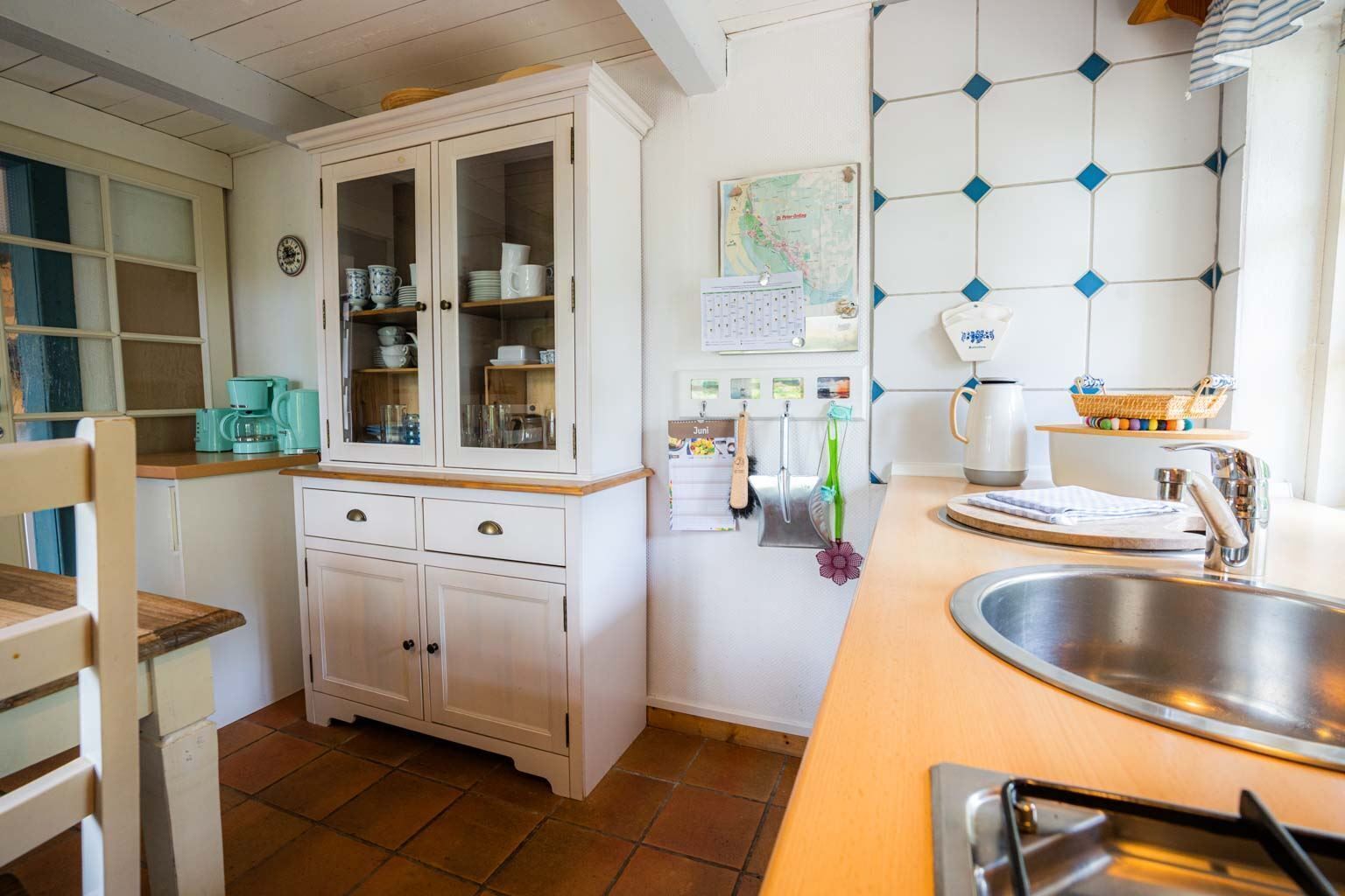 A kitchen with white cabinets, a sink, a coffee maker, and a calendar on the wall.
