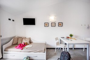 A room with a bed, a TV, a dining table, chairs, and a backpack.