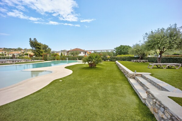 A landscaped area with a swimming pool, a stone retaining wall, and a picnic table.