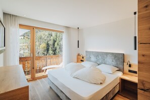 Une chambre dotée d’un grand lit, d’une tête de lit en bois, de tables de chevet, d’un bureau et d’une porte-fenêtre coulissante donnant sur un balcon.