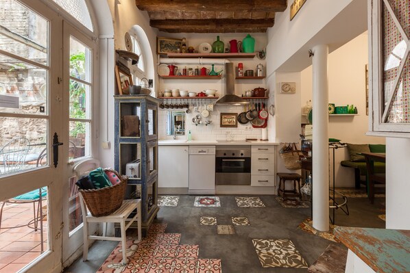 A compact kitchen with white cabinets, a dishwasher, and a variety of kitchenware on shelves.