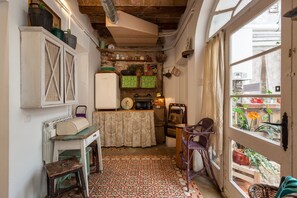 A compact kitchen with a tiled floor, a refrigerator, a microwave, and a table with a lace tablecloth.
