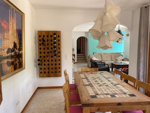 A dining area with a wooden table and chairs, a chessboard, a wine rack, and a framed picture on the wall.