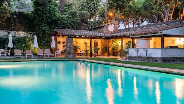 A swimming pool with lounge chairs and umbrellas, surrounded by a building with stone walls and a tiled roof.